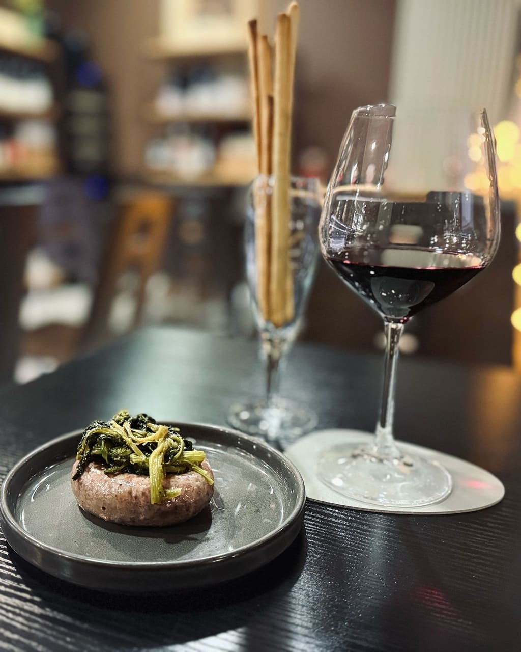 Un tortino di carne con verdure saltate sopra, grissini e un calice di vino rosso