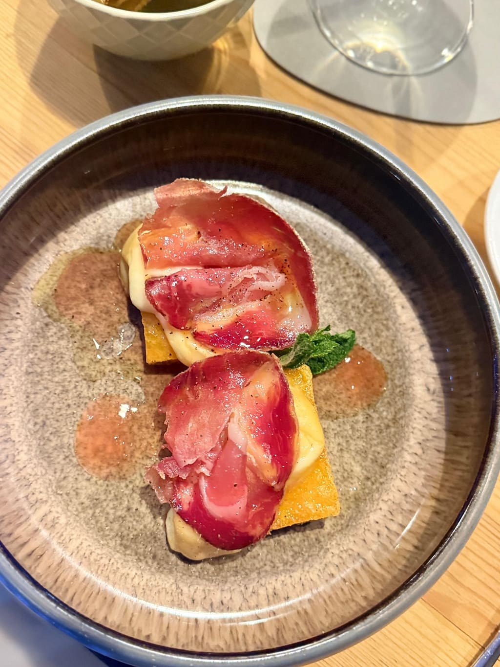 Due quadrotti dorati con formaggio fuso e fette di salume, in un piatto di ceramica